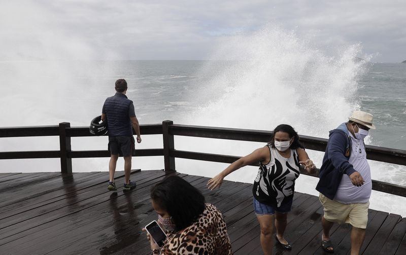Personas con mascarillas salen corriendo de la cubierta cuando las olas golpean las rocas en la playa de Leblon en medio del brote de coronavirus en Río de Janeiro, Brasil. 28 de mayo de 2020. REUTERS/Ricardo Moraes