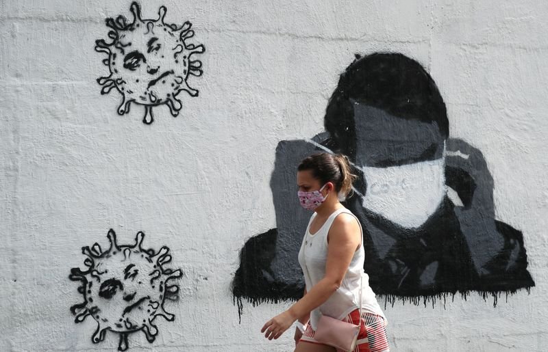Una mujer pasa por delante de un grafiti que muestra al presidente de Brasil, Jair Bolsonaro, ajustando su máscara protectora en Río de Janeiro el 2 de julio de 2020. REUTERS/Sergio Moraes