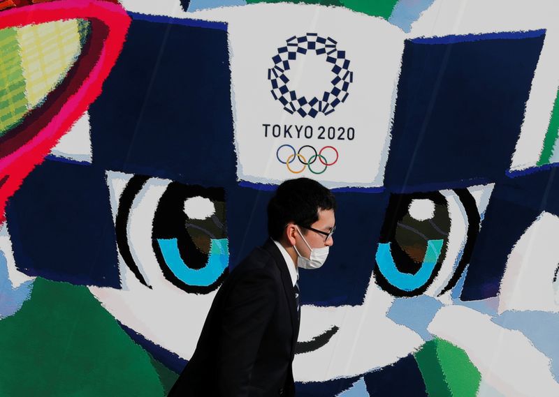 Un hombre con una mascarilla delante de un gran cartel que muestra a la mascota de los Juegos Olímpicos de Tokio 2020, Miraitowa, en Tokio, Japón, el 4 de junio de 2020. REUTERS/Kim Kyung-Hoon